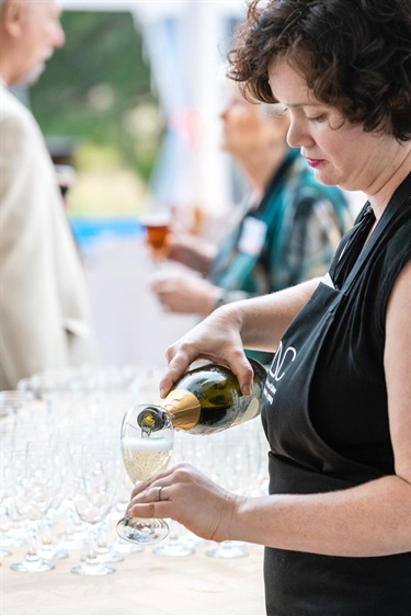 Person in black dress pouring a glass of champaigne