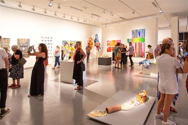 A crowd admires various exhibits at an opening night