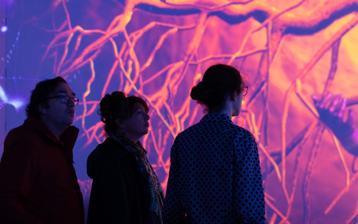 Three people engage with an immersive purple artwork. 